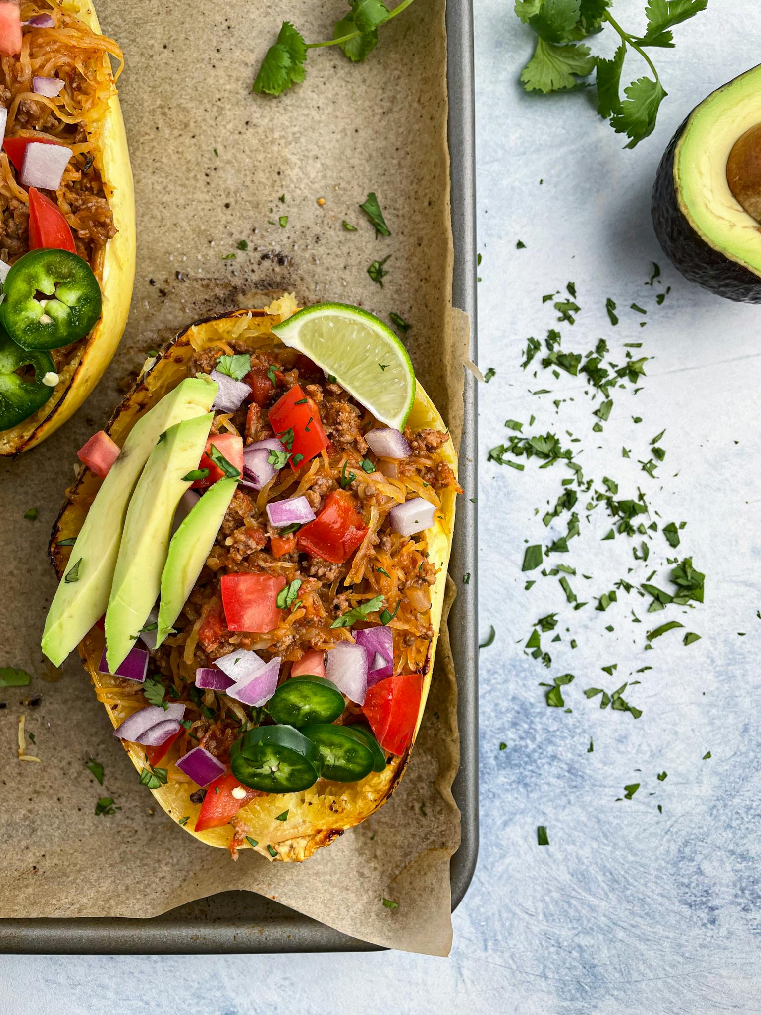 Taco stuffed spaghetti squash on a baking sheet with toppings